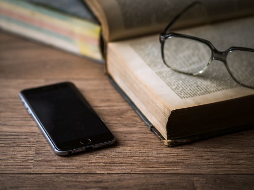 An open book, eyeglasses, and smartphone on a wooden desk, illustrating a classic study setting.